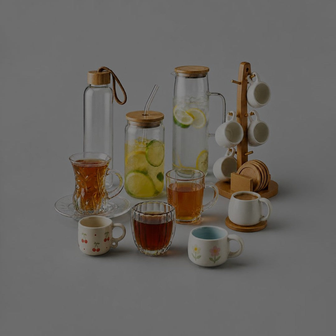 Glass water bottle with strap, glass cup with bamboo lid and straw, glass jug with lemon water, tea glasses, floral mugs and white mugs on a bamboo mug tree