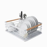 White metal dish drying rack with bamboo handles holding white plates, bowls and cutlery in a utensil holder