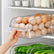 Clear plexi fridge organizer bins holding eggs and cucumbers inside a refrigerator