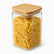 Square glass storage jar with bamboo lid filled with penne pasta