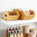 Two bamboo bins with cut-out side handles on a white shelf holding walnuts and bagged cashews, above a rack of spice jars and tan canisters
