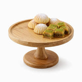 Round bamboo cake stand on a pedestal with ma'amoul cookies and pistachio baklava