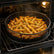 Black mesh air fryer basket and tray filled with crispy fries inside an open oven