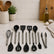 11 black silicone cooking utensils with steel handles laid out on a white marble kitchen counter