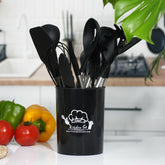 Black silicone cooking utensils standing in their black holder on a kitchen counter next to tomatoes and peppers
