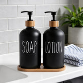 Matte black soap and lotion pump bottles with bamboo collars on an oval bamboo tray on a white bathroom countertop beside a striped towel and a green plant