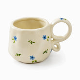 Cream ceramic mug with tiny painted blue flowers, green sprigs and a looped ring handle
