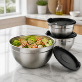 Stainless steel bowl filled with fattoush salad beside its black lid and 2 stacked lidded bowls on a marble kitchen counter