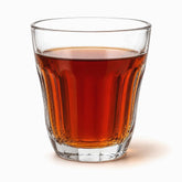Single clear flared paneled tea glass filled with hot red tea, long panels visible through the tea