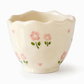 Cream handleless ceramic cup with wavy rim, small painted pink flowers and tiny pink hearts