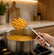 Hand lifting golden fries out of hot oil with a stainless steel spider skimmer over a pot