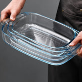 Hands holding 3 nested rectangular glass baking dishes by their textured handles