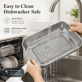 Hands holding a perforated stainless steel tray under a running tap with water draining through the holes and a dishwasher in the background
