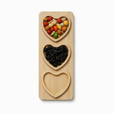 Rectangular bamboo board with 3 removable heart-shaped plates holding coated peanuts and raisins, one plate empty
