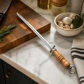 Knife sharpening steel with wooden handle on a marble kitchen counter beside a wooden cutting board and garlic