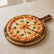 Sliced margherita pizza with basil on a round acacia wood board with handle on a stone counter