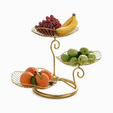 Gold 3-tier metal fruit stand with leaf-shaped wire baskets holding grapes, bananas, green apples and oranges