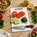 White plastic cutting board with sliced tomatoes, cucumber, chopped parsley and a chef's knife on a kitchen counter