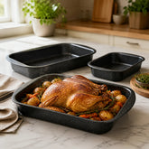 Roasted whole chicken with potatoes and carrots in a granite baking pan with two smaller pans on a marble counter