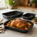 Roasted whole chicken with potatoes and carrots in a granite baking pan with two smaller pans on a marble counter