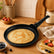 Golden crepe in a granite crepe pan on a wooden counter next to folded crepes with strawberries and blueberries