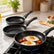 Fried eggs and cherry tomatoes in a granite frying pan on a gas stove with two more pans on a marble counter