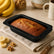 Freshly baked banana bread in a black granite loaf pan with bananas, walnuts and coffee