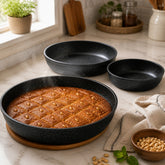 Baked namoura cut into diamonds in a granite round pan with two smaller pans on a marble counter