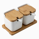 2 white porcelain canisters with bamboo lids and white spoons on a bamboo tray