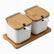 2 white porcelain canisters with bamboo lids and white spoons on a bamboo tray
