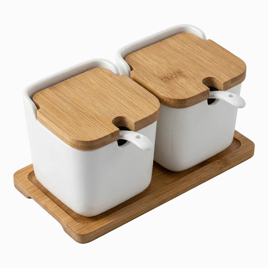 2 white porcelain canisters with bamboo lids and white spoons on a bamboo tray