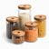 5 ribbed glass jars with burnt wood lids filled with rice, coffee beans, almonds, lentils and pasta