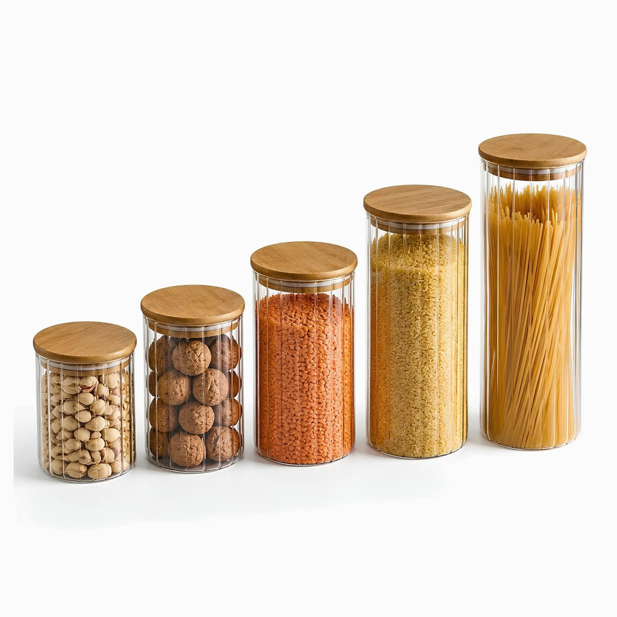 5 ribbed glass jars with bamboo lids in 5 heights filled with pistachios, walnuts, red lentils, bulgur and spaghetti