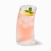 Tall curved ribbed glass with pink rose-water lemonade, ice, lemon slice and mint