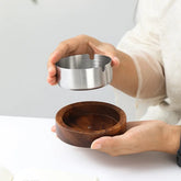 Hands lifting the removable stainless steel bowl out of the round wooden ashtray base