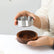Hands lifting the removable stainless steel bowl out of the round wooden ashtray base