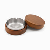 Stainless steel ashtray with 3 cigarette notches in a round wooden base, wooden lid beside it
