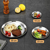Small, medium and large stainless steel plates on a dark slate table with their diameters of 14, 23 and 30 centimeters marked, holding olives, chicken wings and spaghetti with steak