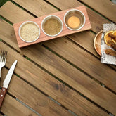 Top view of wooden stand with 3 steel cups of sesame, spices and sauce next to a food plate