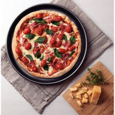 Prosciutto pizza with cherry tomatoes and basil in a graphite pizza pan on a linen towel