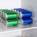Two clear can organizers holding green and blue drink cans on a fridge shelf