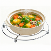 Ceramic pot of vegetable soup resting on a round stainless steel wire trivet