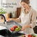 Woman in a linen apron rinsing apples and grapes in a perforated stainless steel tray at a kitchen sink