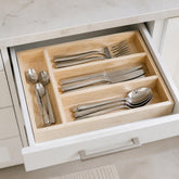 Wooden cutlery organizer in an open white kitchen drawer holding forks, knives and spoons