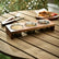 Wooden stand with 3 steel cups of sesame, spices and sauce on a garden table