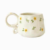 Cream ceramic mug with tiny painted yellow flowers, green sprigs and a looped ring handle