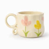 Cream ceramic mug with painted pink and yellow tulips and a looped ring handle